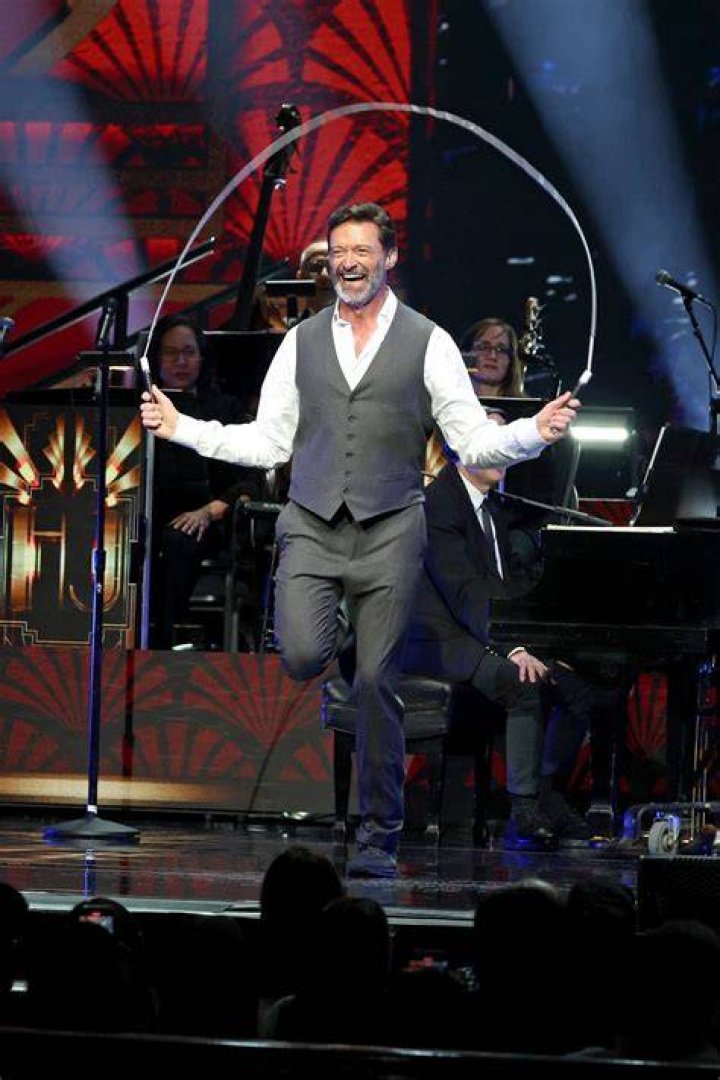 Hugh Jackman holding three fingers up next to wife Deborra-Lee in a blue outfit